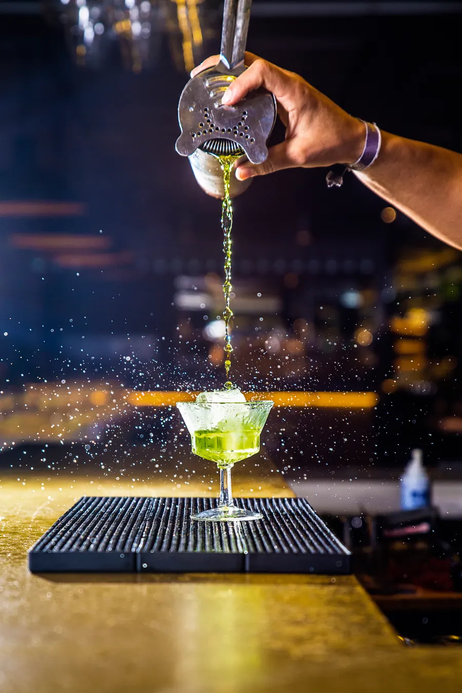 Barmen sipa zeleni koktel kroz cediljku u čašu na šanku