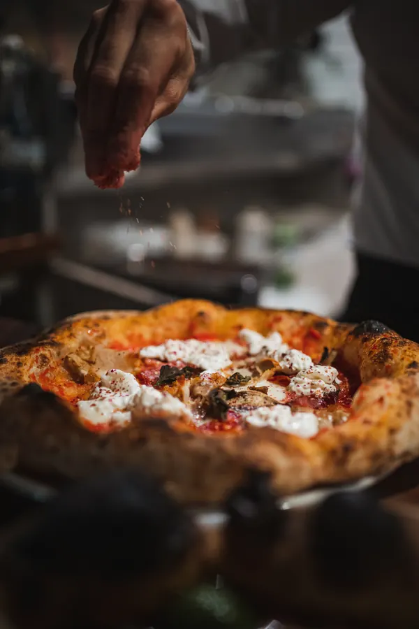 Napolitanska pizza sa sirom, a iznad nje ruka posipa začin